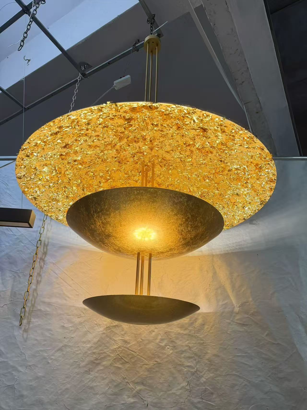 Gold luminous disc pendant with two curved metal forms below during a workshop test