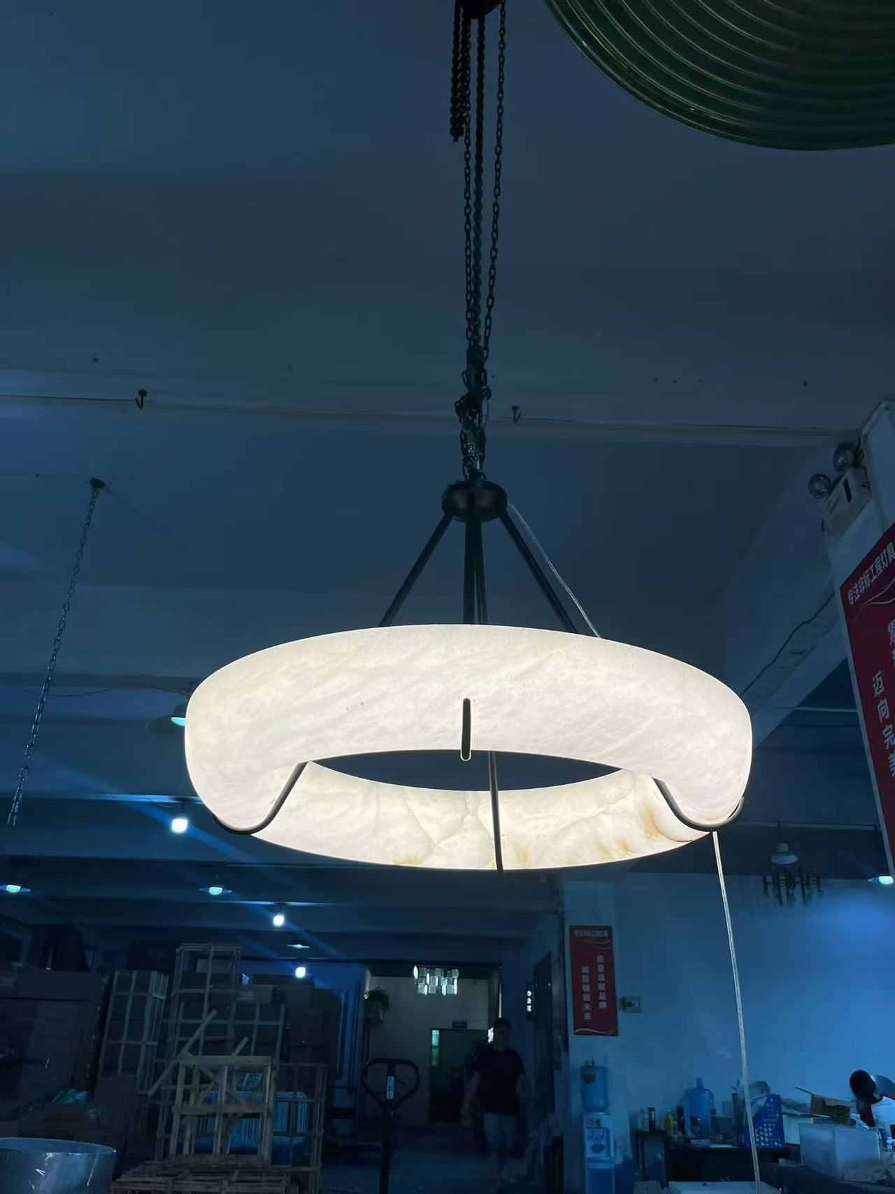 Broad illuminated ring suspended beneath a dark metal structure in the workshop