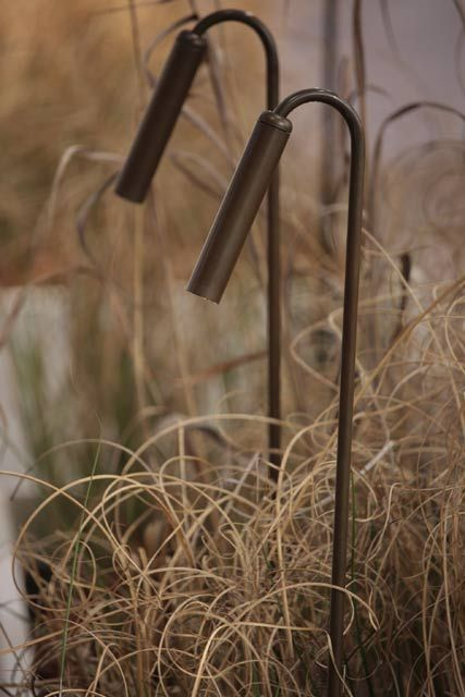 Two custom bronze gooseneck garden lights among ornamental grasses at dusk.