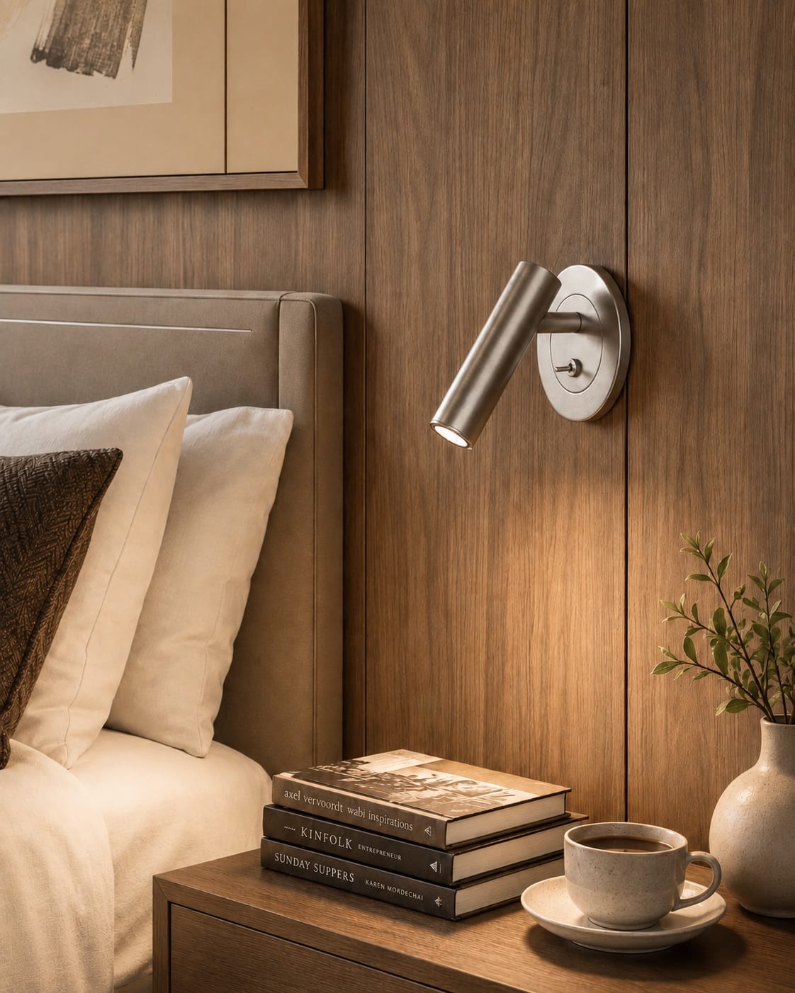 Adjustable dark metal bedside spotlight beside an upholstered hotel headboard
